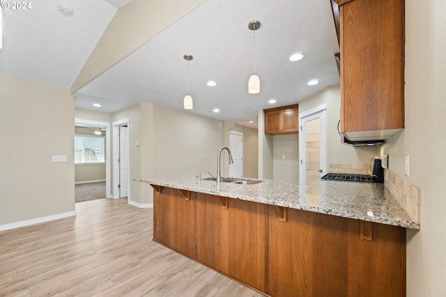 kitchen with sink, kitchen peninsula, hanging light fixtures, and light hardwood / wood-style flooring