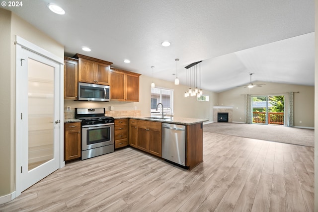 kitchen with kitchen peninsula, stainless steel appliances, vaulted ceiling, sink, and hanging light fixtures