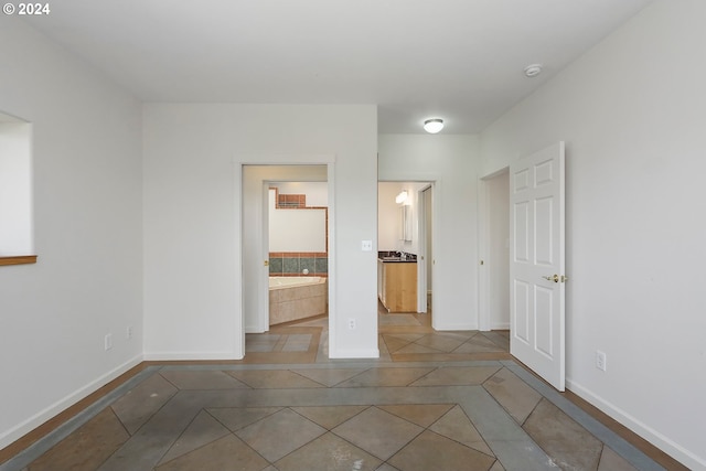 unfurnished bedroom featuring ensuite bath, tile patterned flooring, and baseboards