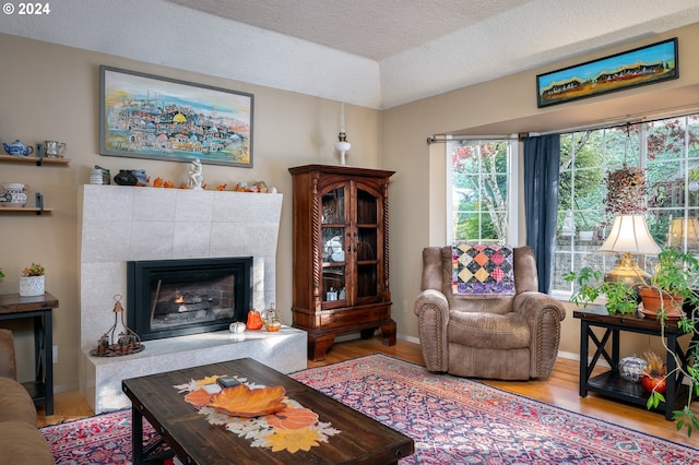 living room featuring a tile fireplace, a textured ceiling, and light hardwood / wood-style flooring