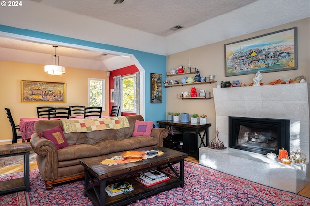 living room with hardwood / wood-style floors, a textured ceiling, and a tiled fireplace