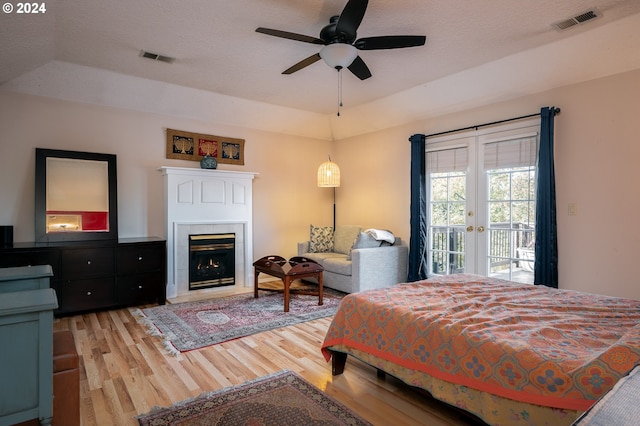 bedroom featuring access to exterior, ceiling fan, a tray ceiling, a fireplace, and light wood-type flooring