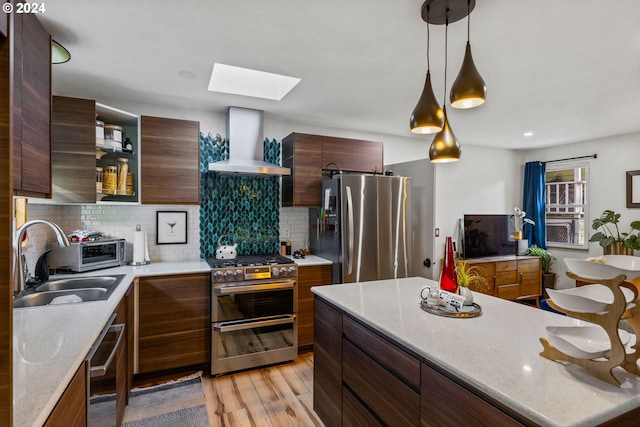 kitchen with appliances with stainless steel finishes, a skylight, light wood-type flooring, hanging light fixtures, and wall chimney exhaust hood