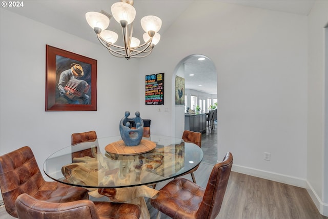 dining room featuring arched walkways, lofted ceiling, a notable chandelier, wood finished floors, and baseboards