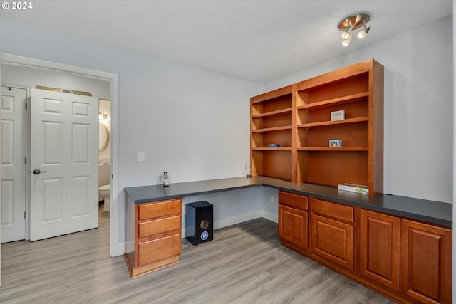 home office with light wood finished floors, baseboards, and built in study area