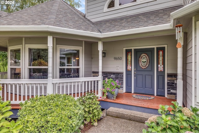 view of exterior entry with a porch and roof with shingles