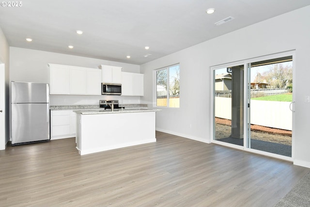 kitchen featuring light hardwood / wood-style floors, white cabinetry, appliances with stainless steel finishes, and an island with sink