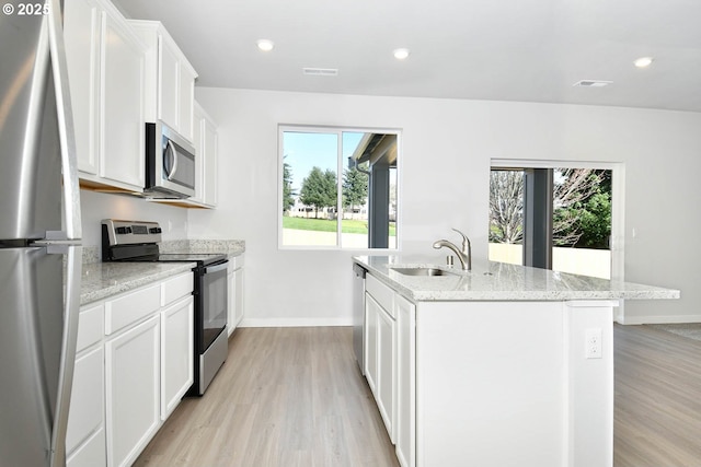 kitchen featuring sink, white cabinets, light stone countertops, an island with sink, and stainless steel appliances