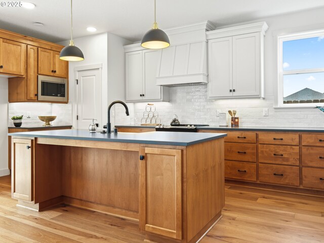 kitchen featuring stainless steel microwave, pendant lighting, an island with sink, and white cabinets