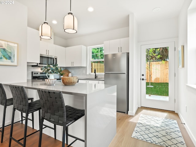 kitchen with stainless steel appliances, white cabinetry, decorative light fixtures, and a breakfast bar area