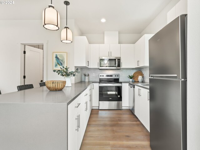 kitchen with wood-type flooring, decorative backsplash, stainless steel appliances, pendant lighting, and white cabinets