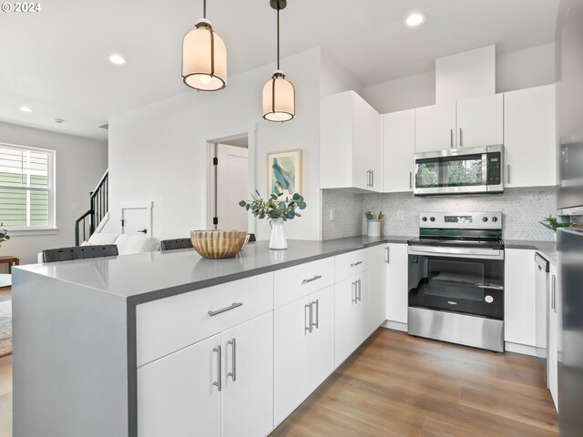 kitchen with appliances with stainless steel finishes, light hardwood / wood-style flooring, decorative light fixtures, white cabinetry, and tasteful backsplash