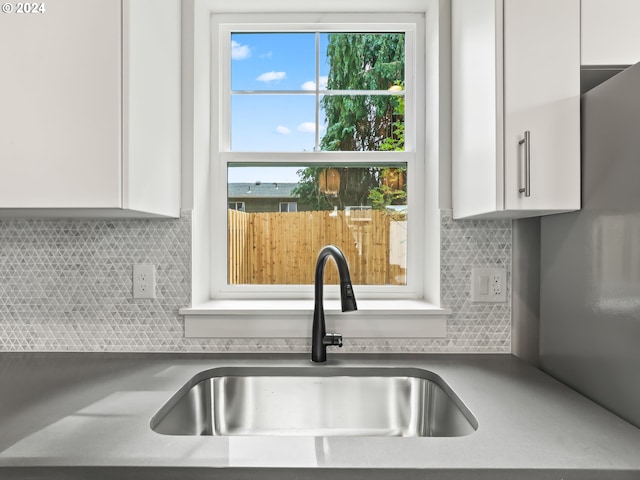 kitchen featuring tasteful backsplash, light countertops, white cabinets, and a sink