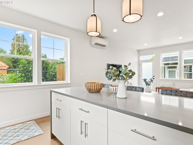 kitchen featuring a wall unit AC, hanging light fixtures, light hardwood / wood-style flooring, and white cabinetry