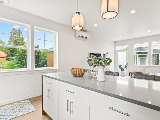 kitchen featuring white cabinets, dark countertops, light wood-style flooring, hanging light fixtures, and an AC wall unit