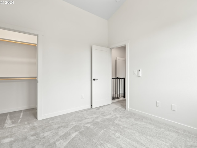 unfurnished bedroom with light colored carpet, baseboards, vaulted ceiling, a closet, and a walk in closet