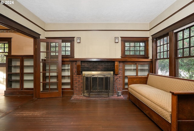 living area with dark wood-type flooring, a textured ceiling, and a brick fireplace