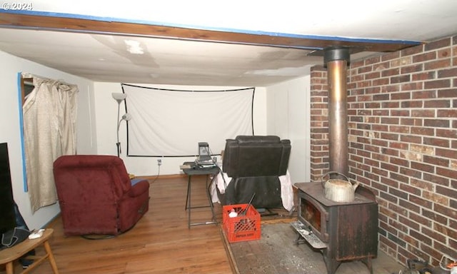 finished basement with brick wall, a wood stove, and wood finished floors