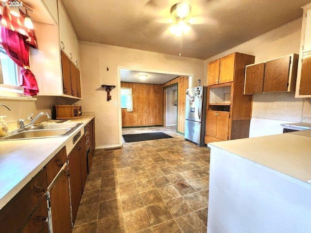 kitchen with light countertops, brown cabinetry, freestanding refrigerator, a sink, and wooden walls