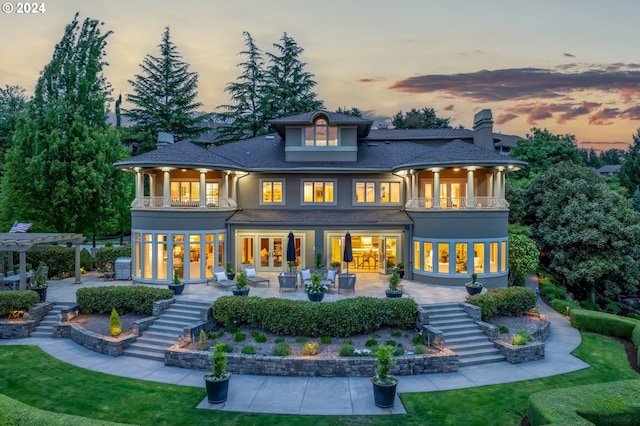 back house at dusk with a balcony, a pergola, a patio area, and french doors