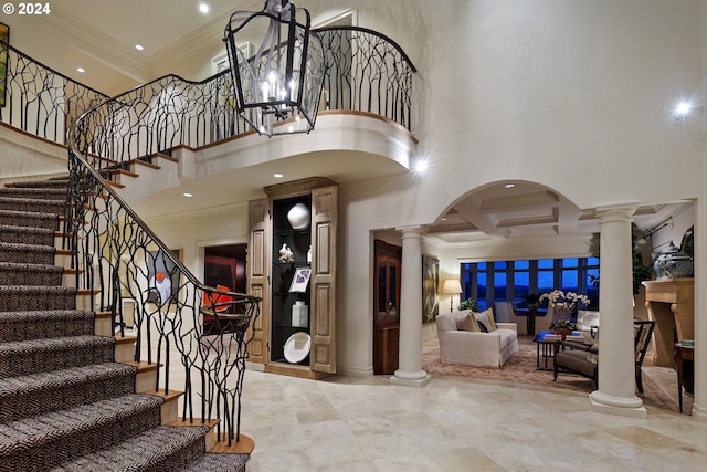 entrance foyer with crown molding, a towering ceiling, and ornate columns