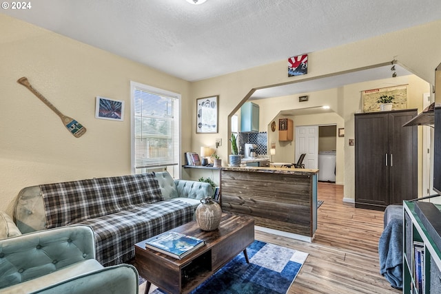 living room featuring washer / clothes dryer, a textured ceiling, and light wood-type flooring