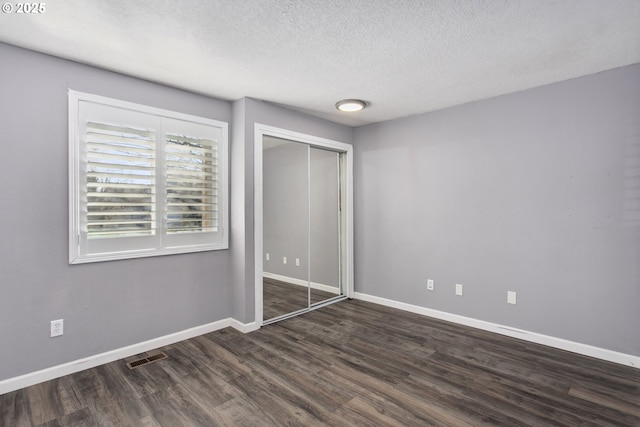 unfurnished bedroom with dark wood-type flooring, a textured ceiling, and a closet