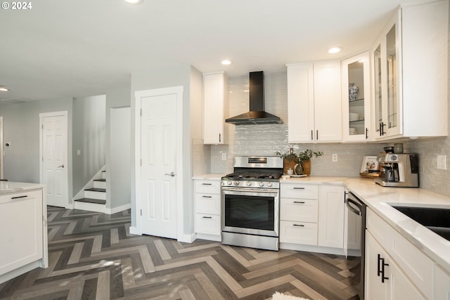 kitchen with white cabinets, dark parquet flooring, wall chimney exhaust hood, and stainless steel appliances