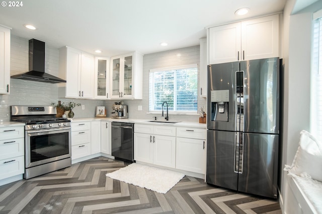 kitchen with dark parquet floors, stainless steel appliances, white cabinetry, and wall chimney range hood