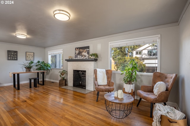 sitting room with a brick fireplace, hardwood / wood-style flooring, and crown molding