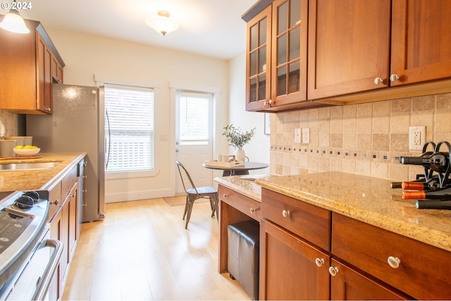 kitchen featuring light stone countertops, backsplash, light hardwood / wood-style floors, stove, and sink