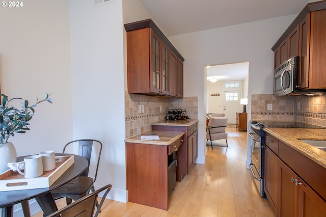 kitchen with backsplash, light stone countertops, stainless steel appliances, and light wood-type flooring