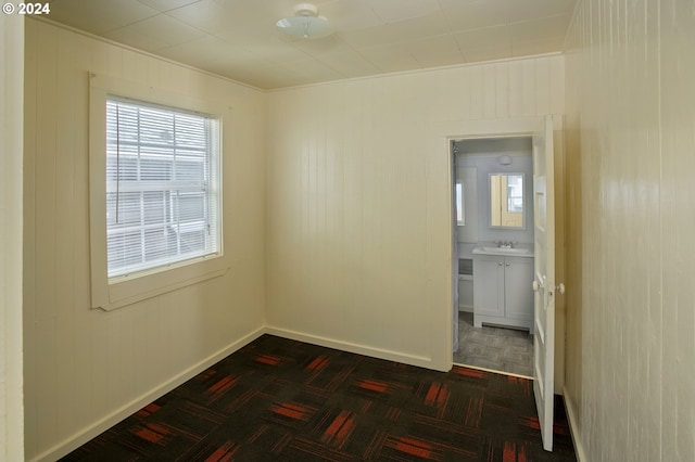 empty room featuring dark parquet flooring, wood walls, and sink