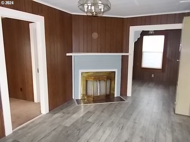 unfurnished living room featuring wood walls, ornamental molding, an inviting chandelier, a fireplace, and hardwood / wood-style floors