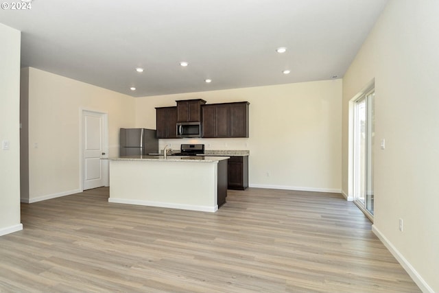 kitchen featuring sink, light wood-type flooring, an island with sink, dark brown cabinets, and stainless steel appliances