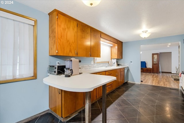 kitchen with a textured ceiling, dishwasher, kitchen peninsula, and dark wood-type flooring