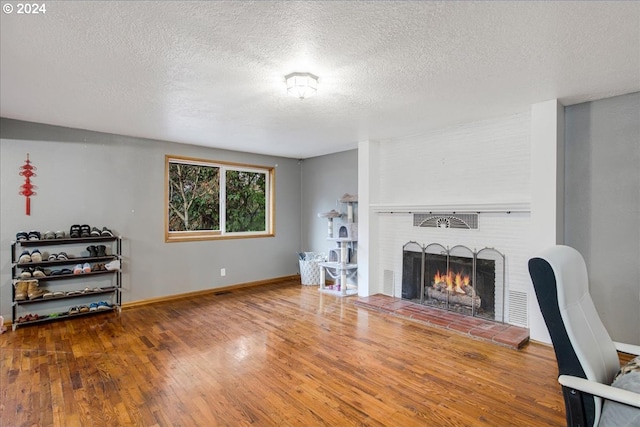 living room featuring a textured ceiling, hardwood / wood-style flooring, and a brick fireplace