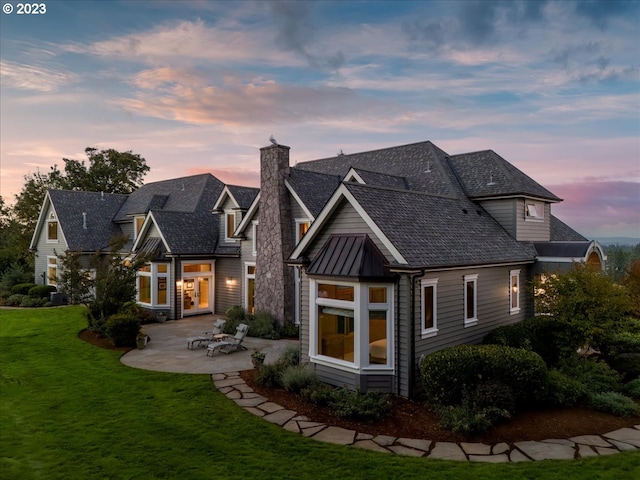 back house at dusk featuring a yard and a patio