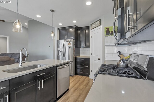 kitchen featuring light wood-type flooring, decorative light fixtures, appliances with stainless steel finishes, and tasteful backsplash