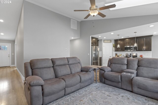 living room with high vaulted ceiling, ceiling fan, crown molding, and light hardwood / wood-style flooring