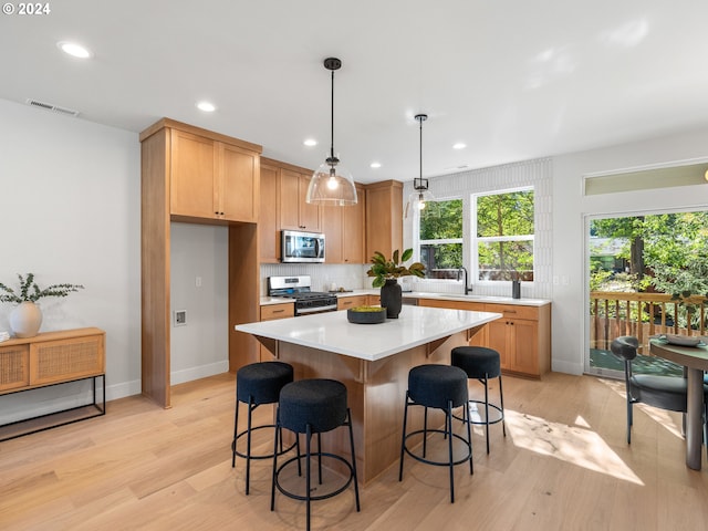 kitchen with pendant lighting, light hardwood / wood-style floors, a center island, backsplash, and appliances with stainless steel finishes