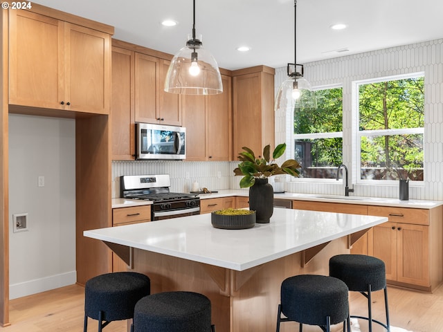 kitchen with light hardwood / wood-style floors, sink, a kitchen island, stainless steel appliances, and decorative light fixtures