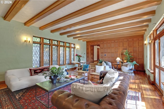 living area with wood-type flooring, a healthy amount of sunlight, and beamed ceiling