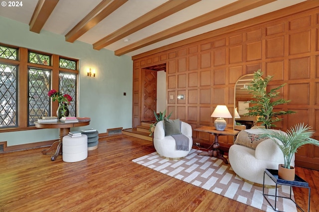 living area with beam ceiling, wood finished floors, visible vents, and baseboards