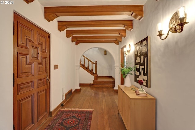 corridor with arched walkways, beam ceiling, hardwood / wood-style flooring, baseboards, and stairs