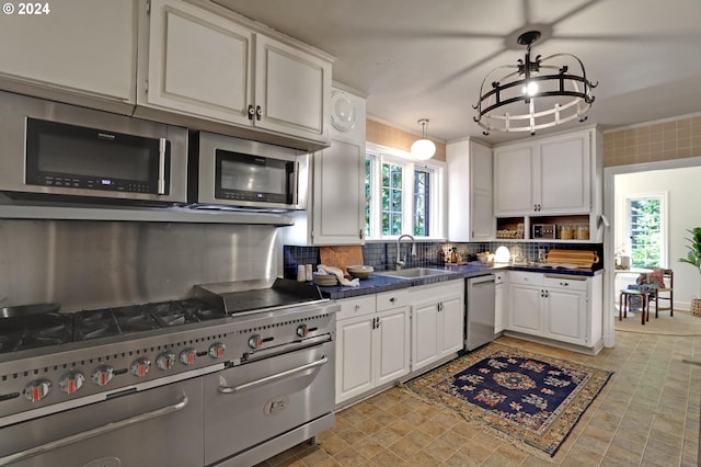 kitchen with stainless steel appliances, dark countertops, decorative backsplash, white cabinets, and a sink