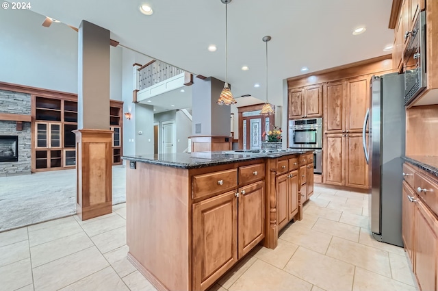 kitchen featuring stainless steel appliances, dark stone counters, a kitchen island, a fireplace, and decorative light fixtures