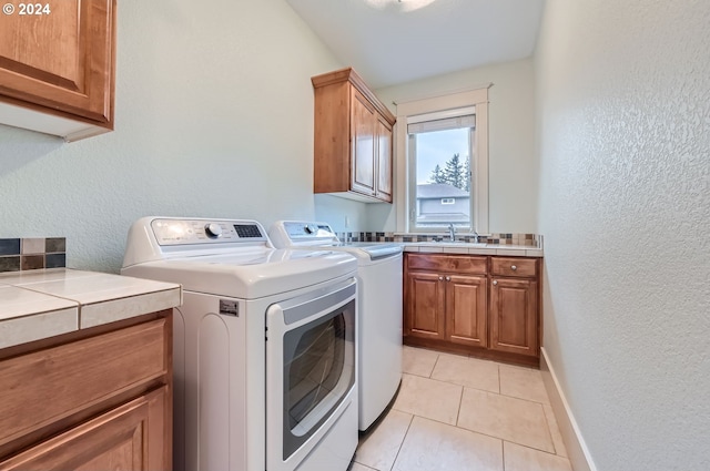 washroom with washing machine and clothes dryer, cabinets, light tile patterned floors, and sink