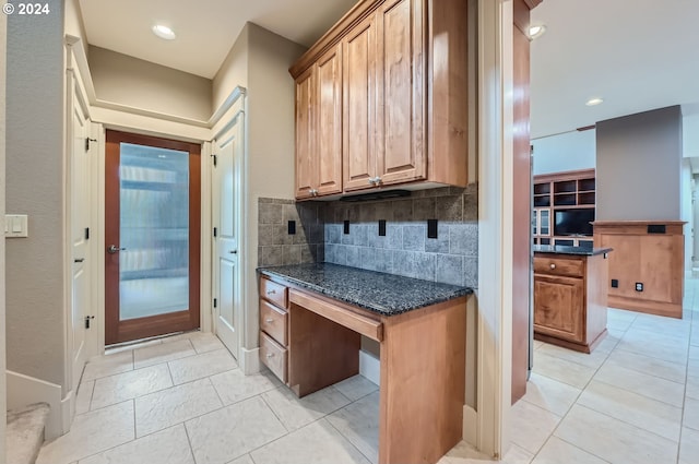 kitchen featuring dark stone counters, built in desk, light tile patterned floors, and tasteful backsplash