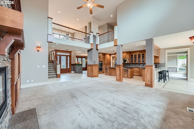 unfurnished living room featuring a high ceiling, a stone fireplace, light carpet, and ceiling fan